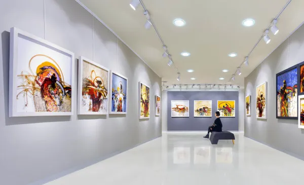 Kunstausstellung mit Sitzmöglichkeit in der Mitte, wo eine Frau sitzt und die Bilder anguckt