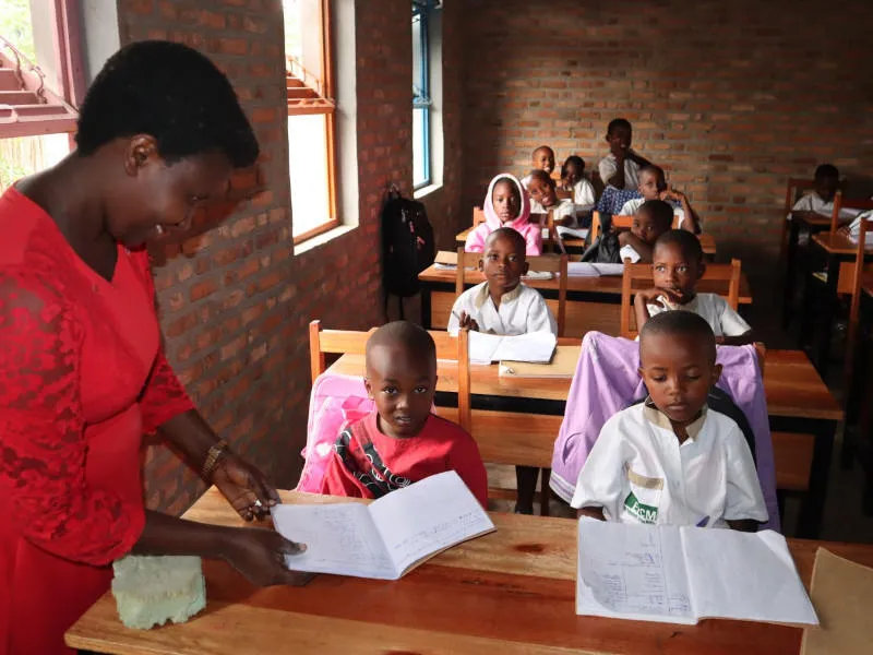 Frau in rotem Oberteil unterrichtet Grundschüler an Zweiertischen in Afrika