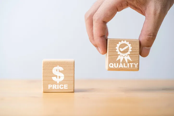 Eine Hand hält das Qualitätssymbol aus Holz, um zwischen Preis und Qualität des Produktkonzepts zu wählen.