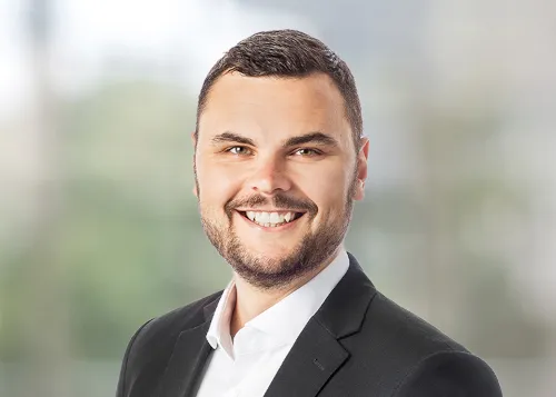 Consultant Heiko trägt ein weißes Hemd mit einem schwarzen Jackett und lächelt breit