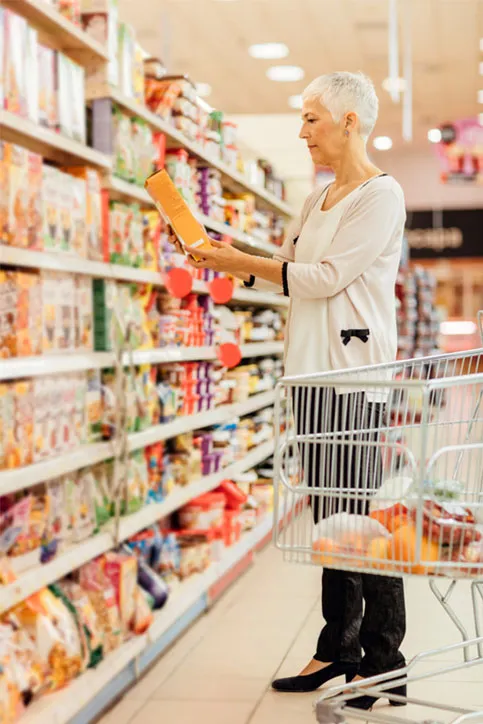 Ältere, gut gekleidete Frau steht im Supermarkt mit ihrem Einkaufwagen bei einem Regal und studiert ein Produkt, welches sie in den Händen hält. Jede Zielgruppe hat unterschiedliche Erwartungen.