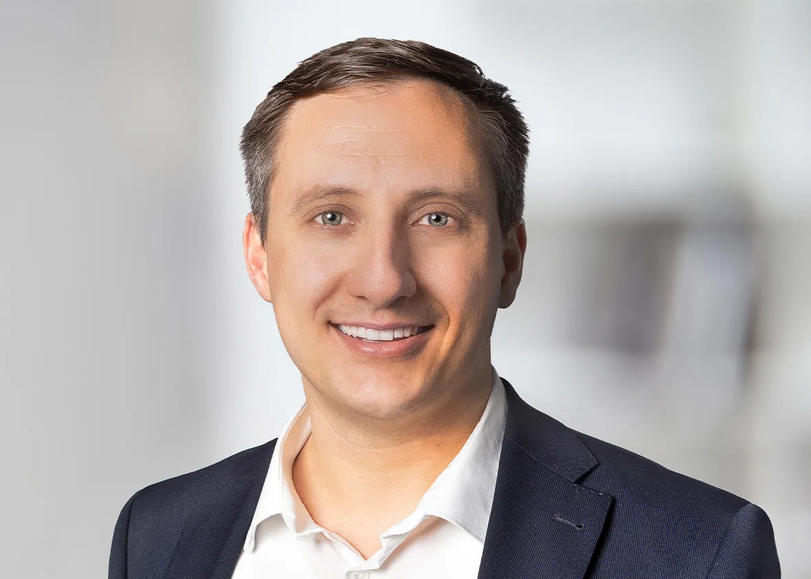 Neuer Associate Partner Martin trägt ein weißes Hemd mit einem dunkel blauem Jackett und lächelt breit