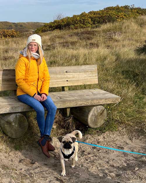 Feizeitbild der R&P Recruiting Coordinator Malien zeigt sie sitzend auf einer Bankin Dünen mit Hund