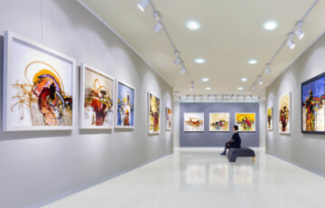 Kunstausstellung mit Sitzmöglichkeit in der Mitte, wo eine Frau sitzt und die Bilder anguckt