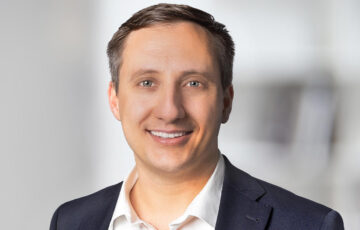 Neuer Associate Partner Martin trägt ein weißes Hemd mit einem dunkel blauem Jackett und lächelt breit