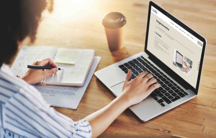Person tippt mit der rechten Hand auf der Tastaur des Laptops und in der linken Hand h&auml;lt sie einen Stift