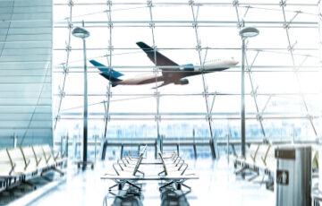 Blick vom Gate durch Glasfenster-Front, wobei gerade ein Flugzeug abhebt.