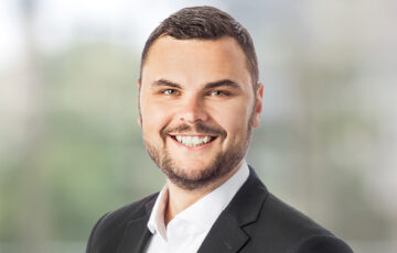 Consultant Heiko trägt ein weißes Hemd mit einem schwarzen Jackett und lächelt breit